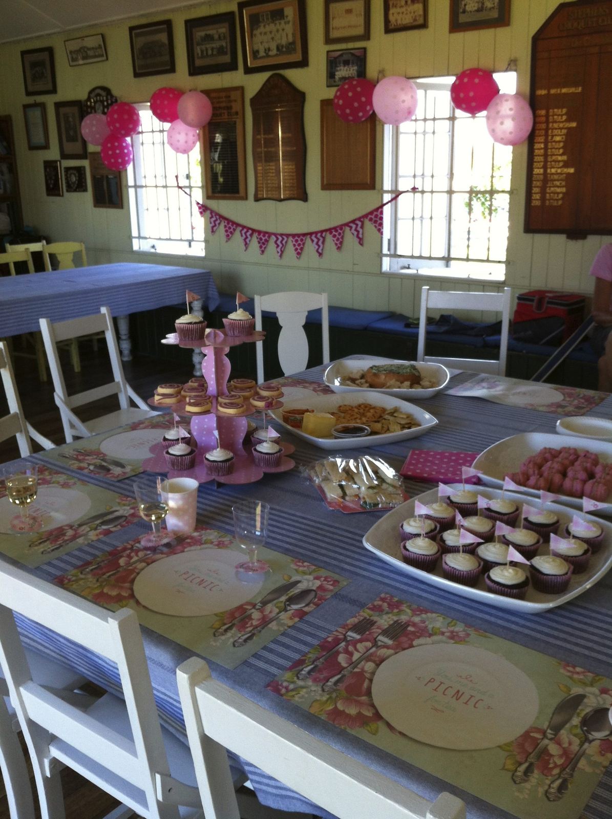 The clubhouse set for a party: a long pink table of cakes and platters, honour boards on the wall