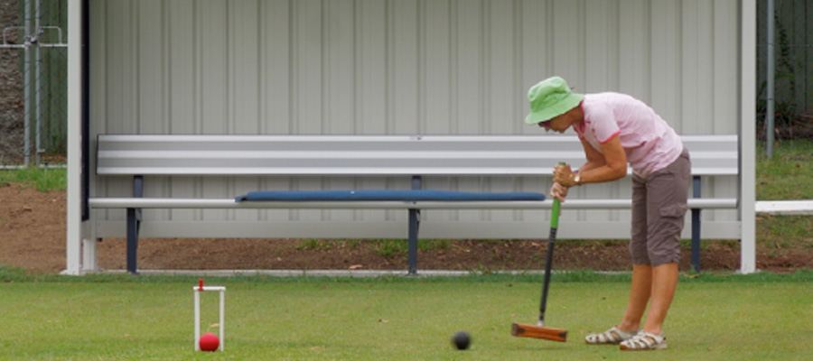 A member in a green hat taking a croquet shot, ball and hoop in front