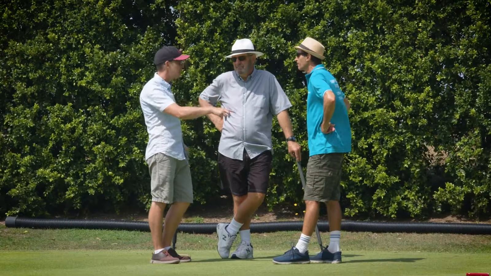 Three players in sun hats talking beside a croquet lawn