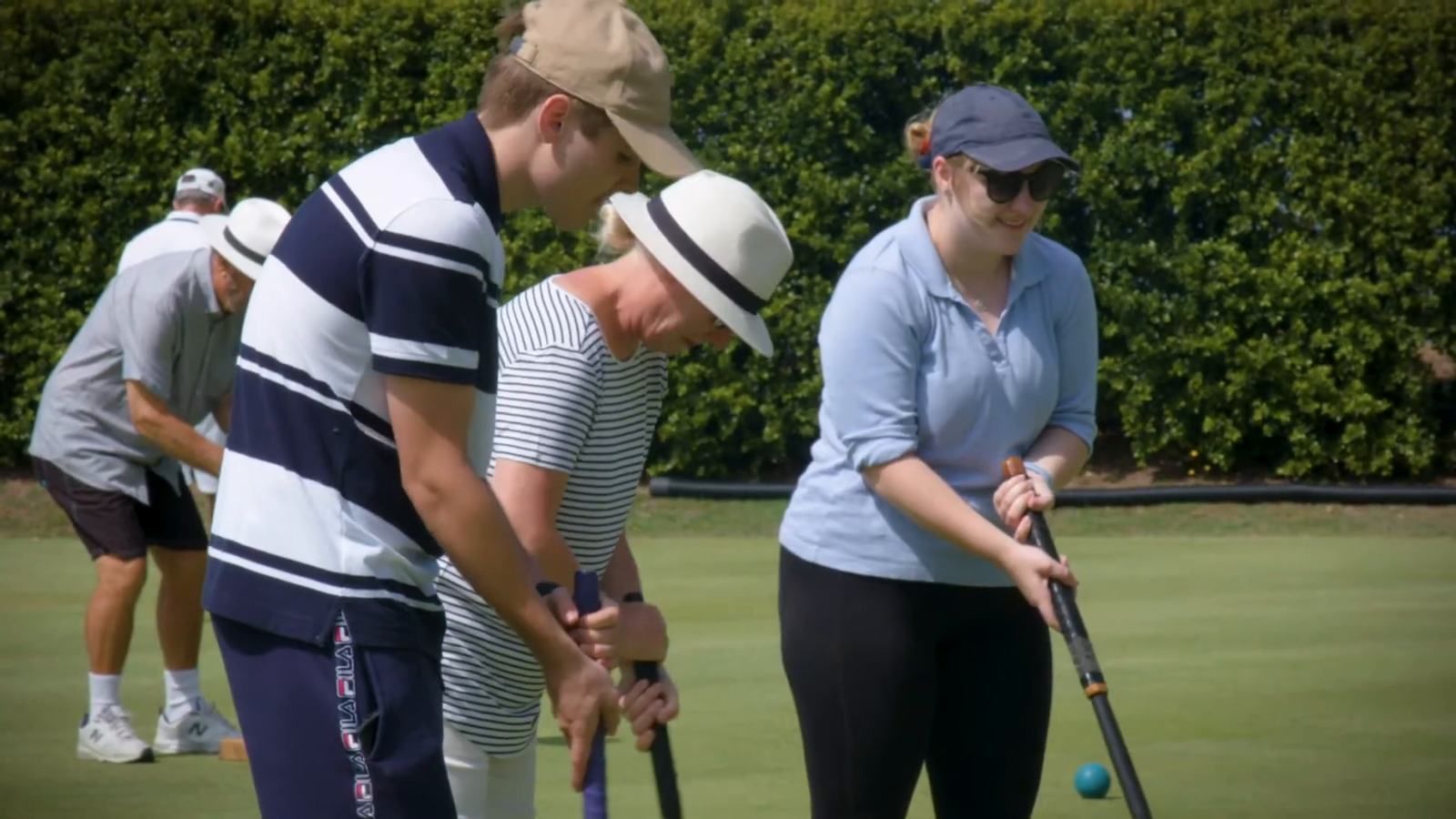 A coach guiding two new players as they hold their mallets