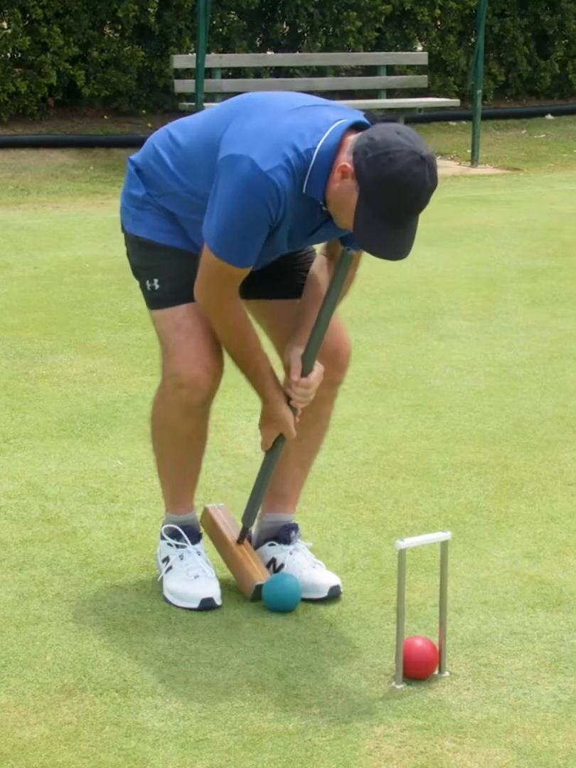 A player in a blue shirt bent over his mallet, lining up a ball at a hoop