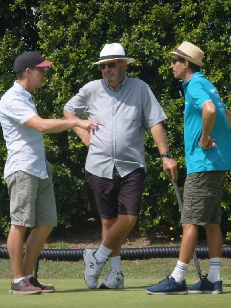 Three players in sun hats talking and laughing beside the lawn
