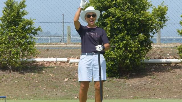 A player in a sun hat waving from the lawn